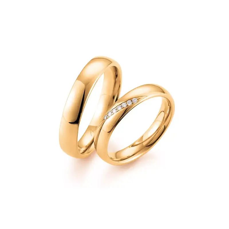 Zwei goldene Ringe liegen nebeneinander. Der eine ist schlicht, der andere hat eine Reihe kleiner, funkelnder Steine.